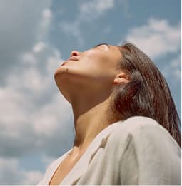 A woman turning her face up to an open sky